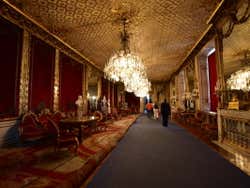 Chandeliers hanging over a long corridor decorated in red and gold