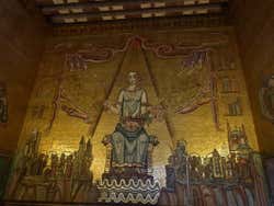 A golden painting of someone sat on a throne holding crown jewels