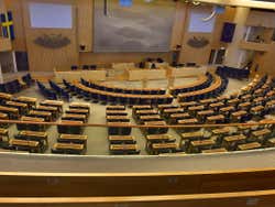 A semi-circular room with lots of desks and chairs facing a small stage